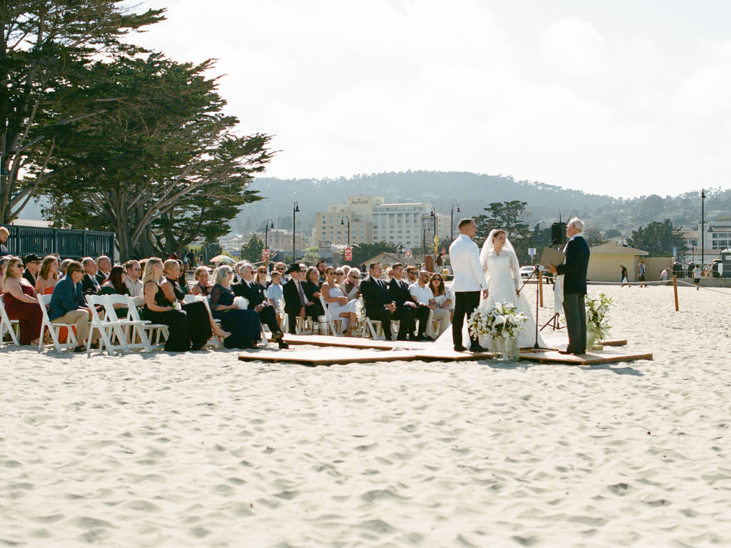 A beach wedding ceremony underway with the Monterey coastline behind