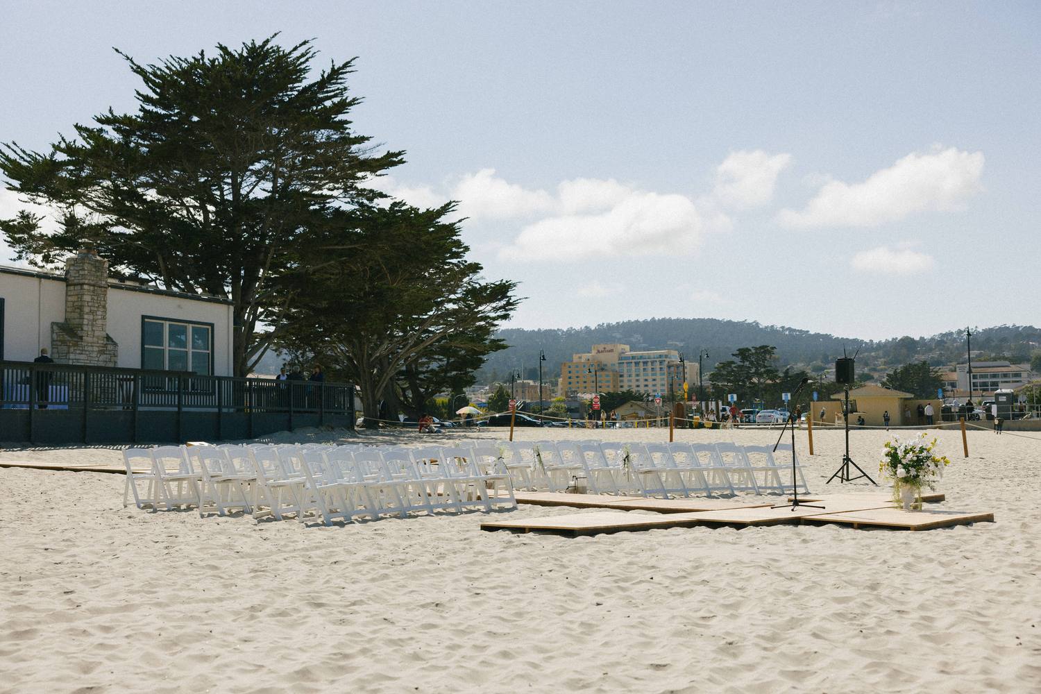 A beach ceremony set on the sand, chairs and a wooden aisle deck with the speaker placed for the wind