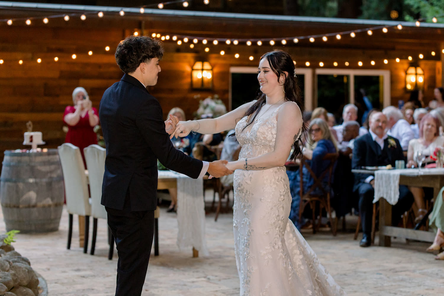 A first dance on the stone patio under string lights, guests watching from their tables beside the lodge